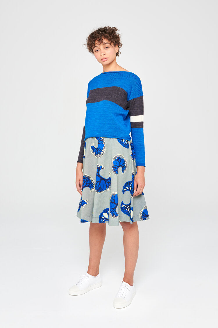 Femme portant un pull en laine merinos extrafine bleu vif, couleur intense et  rayures asymétrique, porté avec une jupe midi.