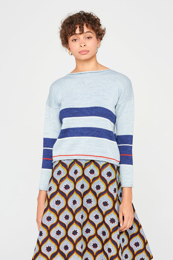 Femme portant un pull en laine merinos extrafine bleu pâle,  rayures marines originales et encolure bateau.