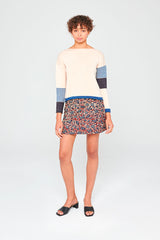 Pull en laine merinos extrafine rosée, couleur douce et rayures asymétriques porté avec une jupe mini.